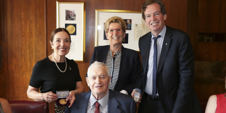 The Rt. Hon. John Turner receives a medal from Premier Kathleen Wynne and John Geiger, CEO of The Royal Canadian Geographical Society.